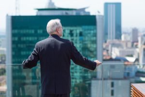 Portrait of senior businessman standing on balcony and looking at city view